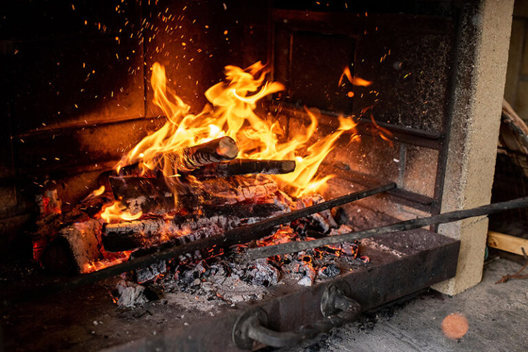 Small logs are burning with ashes underneath it in a fireplace