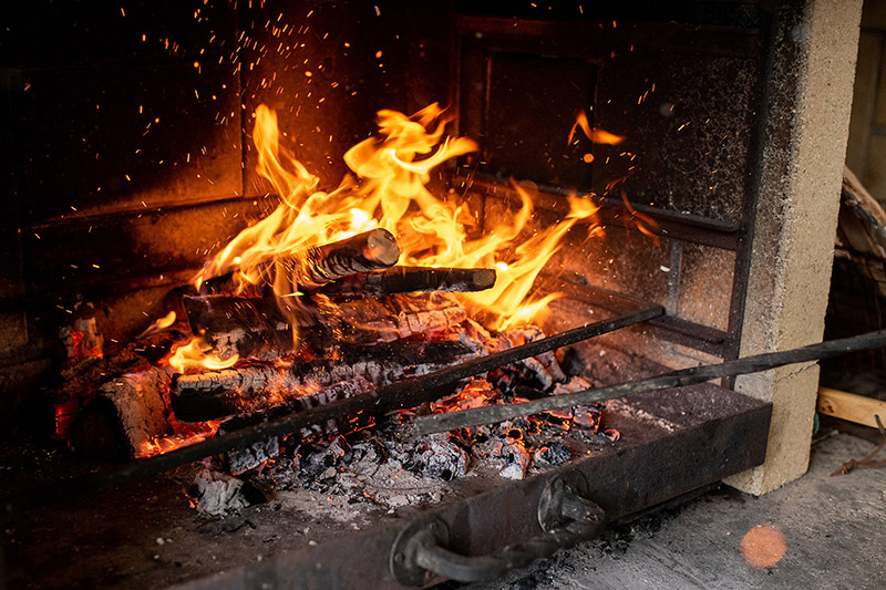 Small logs are burning with ashes underneath it in a fireplace