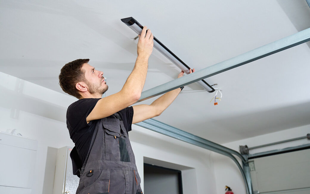 Man in workwear installing a linear LED light fixture on the ceiling indoors. Concept of electrical installation, maintenance work and home renovation.