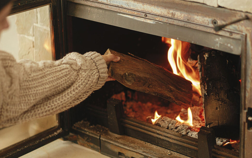Woman is putting a piece of wood into a fireplace