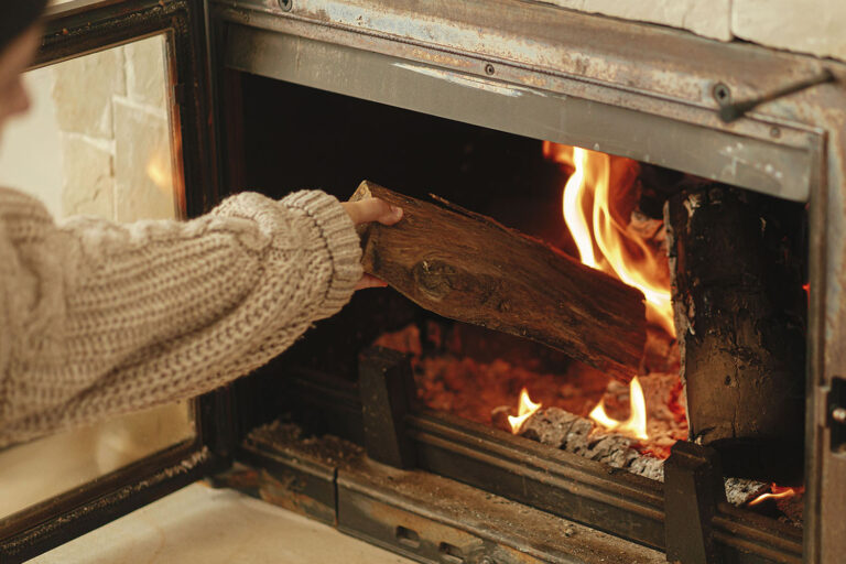 Woman is putting a piece of wood into a fireplace