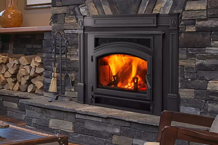 A metal insert fireplace set inside a brick wall, with a pile of firewood beside it.